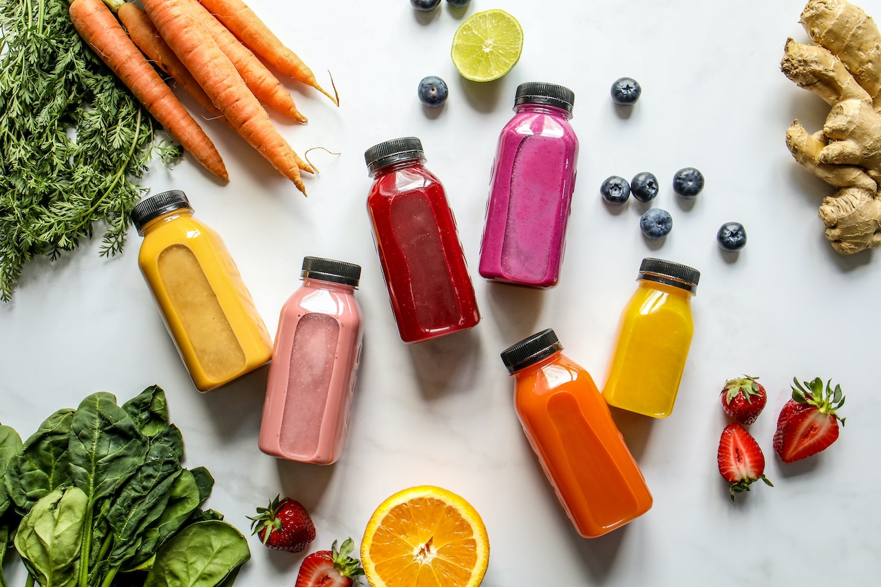 An image of detox juices in different colors with ginger, carrots, strawberry and blackberries
