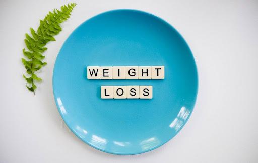 A blue plate with weight loss word in tiles with green leaves on the side